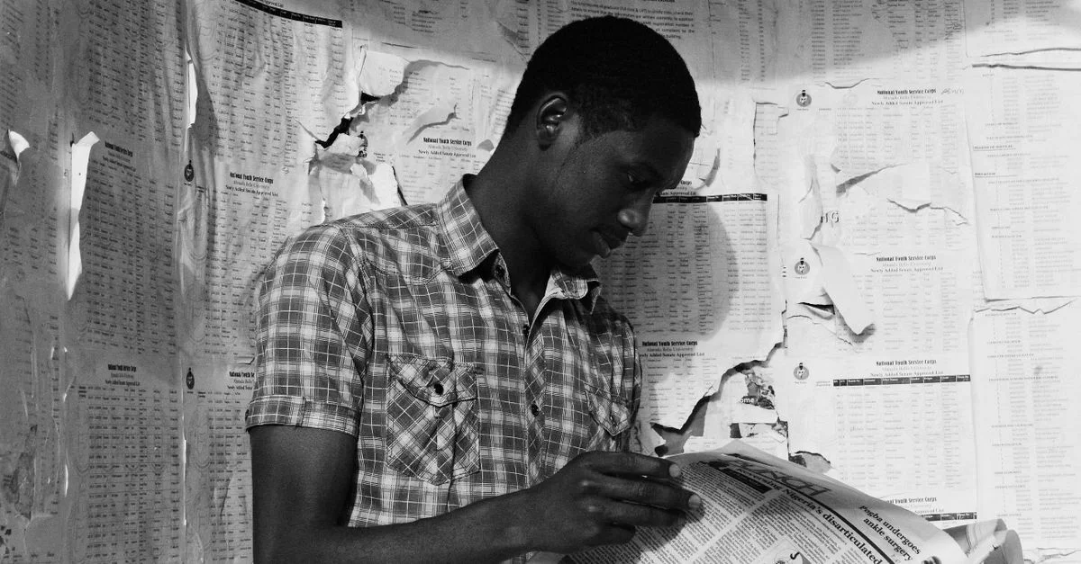 Un homme lit un journal devant un mur couvert de vieilles pages déchirées.